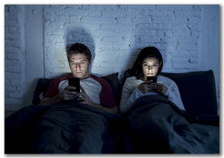 Couple on Bed looking at cell phones not each other